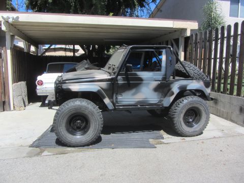 1987 Suzuki Samurai - Side view of a Suzuki Samurai with custom camouflage paint, parked under a carport.