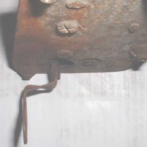 1986 Ford Bronco - This image shows a close-up of a rusty metal component, possibly a bracket or housing, with a bent metal tab extending from it.