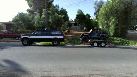1987 Suzuki Samurai - A dark Suzuki Samurai is transported on a U-Haul trailer, towed by a two-tone Ford Bronco.
