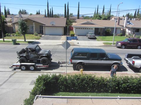 1987 Suzuki Samurai - An off-road vehicle is transported on a trailer, towed by a large SUV on a residential street.