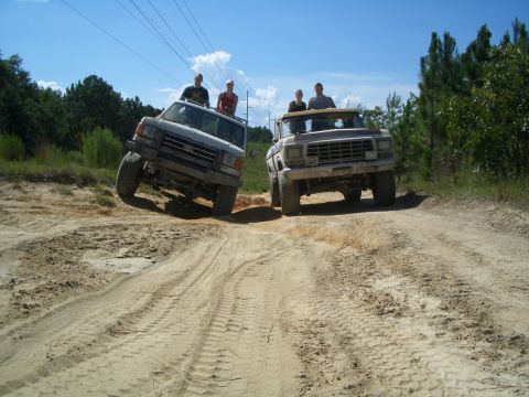 1979 Ford Bronco - Two trucks navigate a sandy off-road path under a clear blue sky.