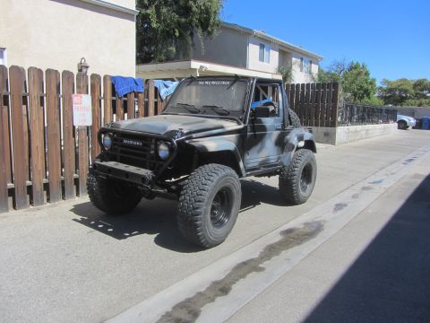 1987 Suzuki Samurai - A modified 1987 Suzuki Samurai with a camouflage paint job and large tires sits in a driveway.