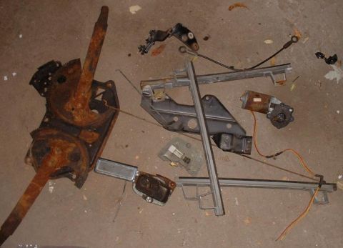 1986 Ford Bronco - Various rusty car parts, including a window regulator and motor, are scattered on a concrete surface.