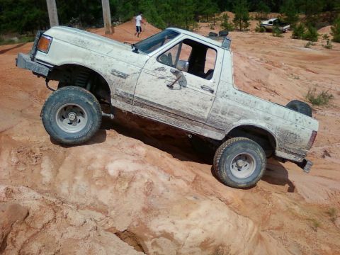 1979 Ford Bronco - This white off-road truck navigates a steep dirt incline, with another vehicle visible in the distance.