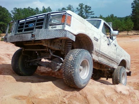 1979 Ford Bronco - This lifted Ford truck is navigating a challenging off-road terrain with its front wheels angled.
