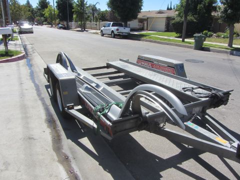 1987 Suzuki Samurai - A U-Haul car trailer is parked on the side of a street in a suburban neighborhood.