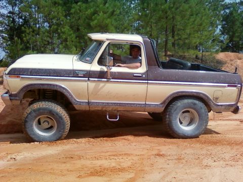 1979 Ford Bronco - A man drives a two-tone Ford Bronco off-road, kicking up dust on a sunny day.