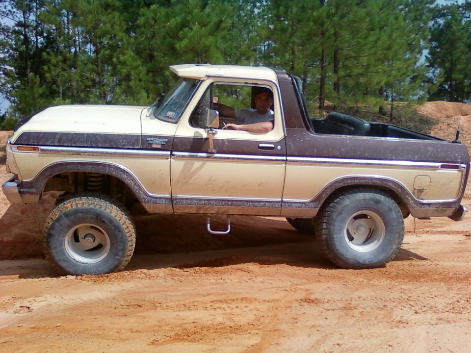 Tan and brown Ford Bronco with a sun visor driving on a dirt road