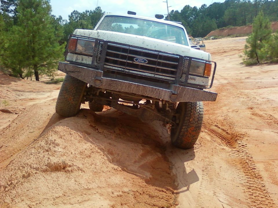 White 1979 Ford Bronco with custom bumper off-roading on a dirt hill
