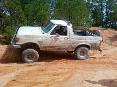1979 Ford Bronco - Mud-covered 1987 Ford F-150 pickup truck navigates an off-road dirt track.