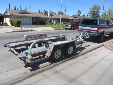 1987 Suzuki Samurai - A pickup truck tows a U-Haul auto transport trailer down a suburban street.