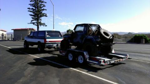1987 Suzuki Samurai - A pickup truck tows a trailer carrying a modified off-road vehicle.