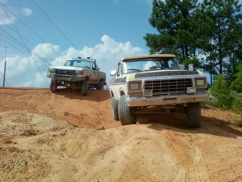 1979 Ford Bronco - Two trucks navigate a sandy incline under a bright blue sky with scattered clouds.