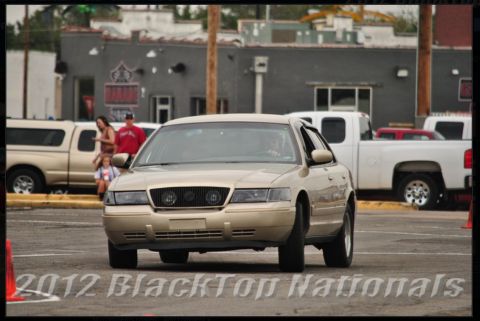 2000 Mercury Grand Marquis - A tan sedan drives forward, with other vehicles and people in the background.