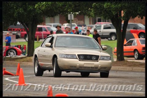 2000 Mercury Grand Marquis - A gold sedan, identified as a 2000 Mercury Grand Marquis, navigates a course with orange cones.