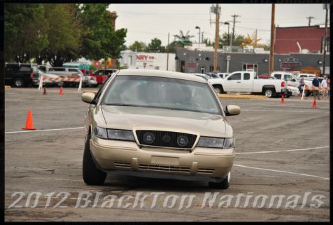 2000 Mercury Grand Marquis - A gold Mercury Grand Marquis is seen from the front in an outdoor parking lot, possibly during an event.