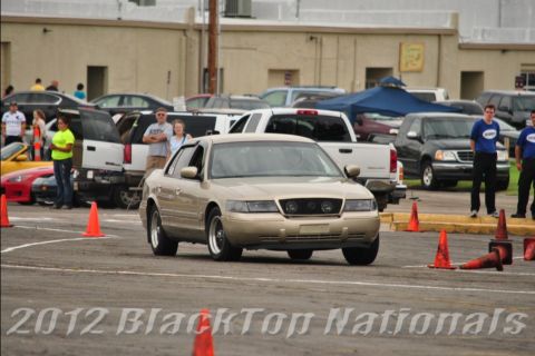 2000 Mercury Grand Marquis - A tan sedan navigates a course marked by orange cones, with other vehicles and spectators in the background.