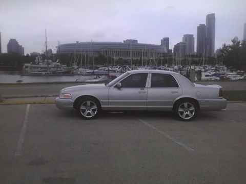 2003 Ford Crown Victoria - A silver 2003 Ford Crown Victoria is parked in a lot with a marina and city skyline in the background.