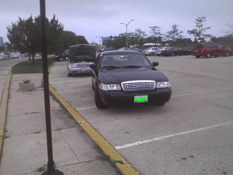 2003 Ford Crown Victoria - A black 2003 Ford Crown Victoria is parked in a lot, with another vehicle's hood open in the background.