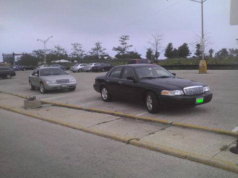 2003 Ford Crown Victoria - Two Ford Crown Victorias are parked in an outdoor lot under an overcast sky.