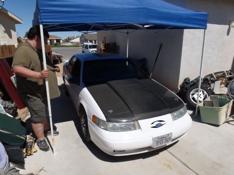 1993 Ford Taurus - A white Ford Taurus with a carbon fiber hood is parked under a blue canopy in a driveway.