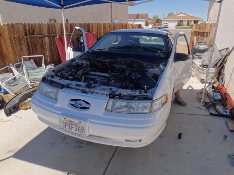1993 Ford Taurus - A white 1993 Ford Taurus is parked outside with its hood open, revealing the engine compartment.