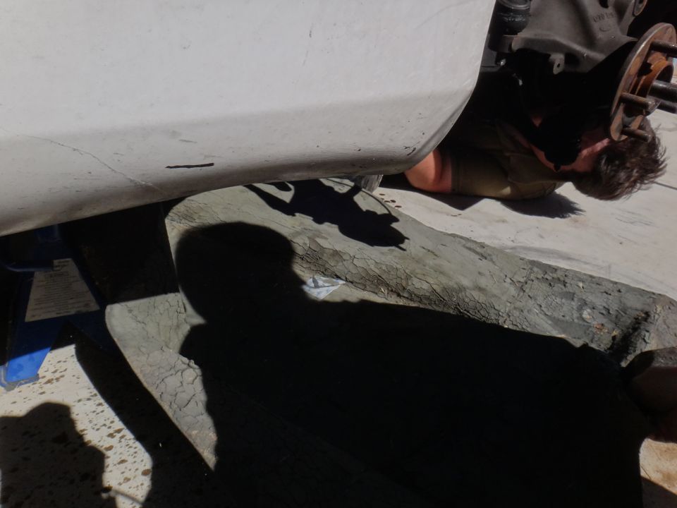 Person lying on ground working on car's front wheel hub assembly. Car body is white