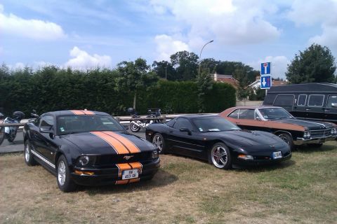 1991 Ford LTD Crown Victoria - A black Ford Mustang with orange racing stripes is parked next to a black Chevrolet Corvette, with other vehicles and motorcycles in the ba…