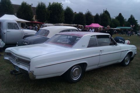 1991 Ford LTD Crown Victoria - A white 1963 Buick Skylark coupe with a patterned roof is seen at an outdoor event with other vehicles.