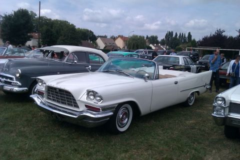 1991 Ford LTD Crown Victoria - This white 1957 Chrysler convertible is parked on grass with other vehicles in the background.