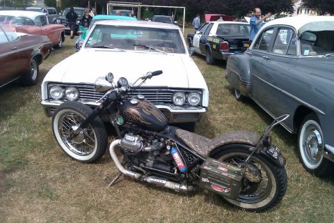 1991 Ford LTD Crown Victoria - A custom motorcycle is parked in front of a white classic car, with other vehicles visible in the background.