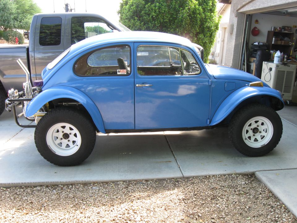 Blue VW Beetle with off-road tires parked next to a pickup truck
