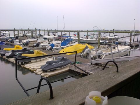 2007 Wellcraft 200 LT Fisherman - Multiple jet skis and boats are moored at a dock in a marina under an overcast sky.