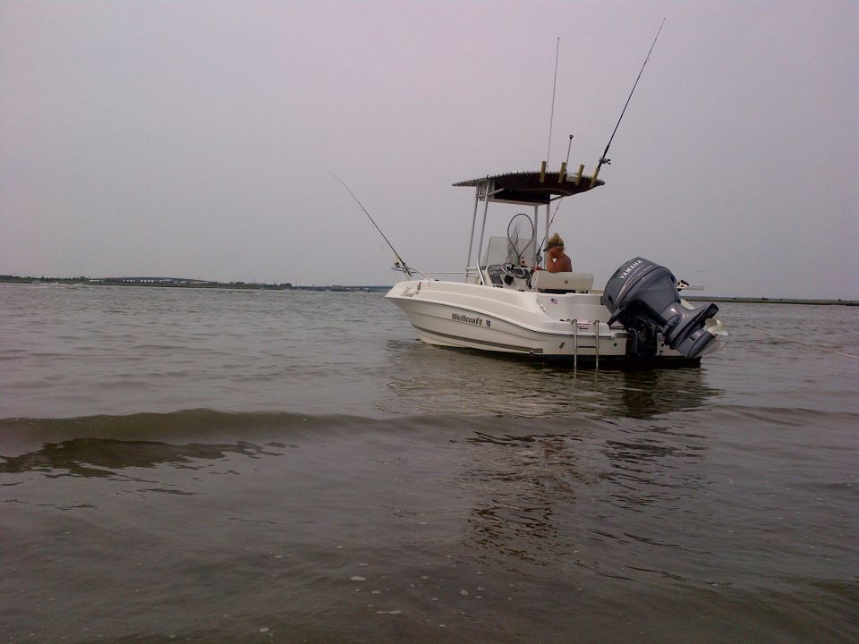 White fishing boat with a T-top and fishing rods, viewed from the side with a person at the helm and a Yamaha outboard motor