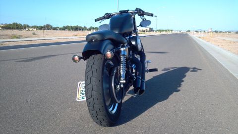 2002 Harley-Davidson XL Sportster - A black motorcycle is viewed from the rear on an empty road under a clear blue sky.
