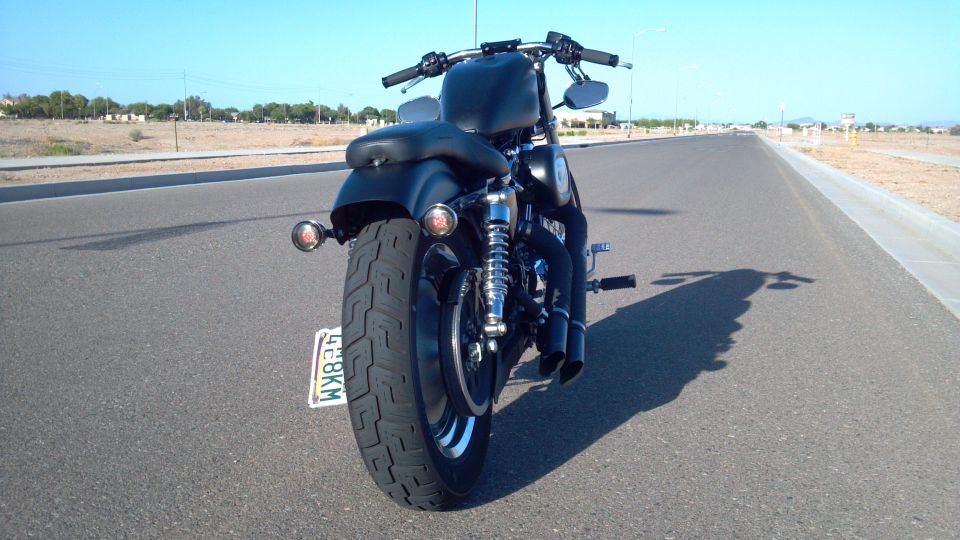 Black motorcycle rear view on asphalt road. Visible license plate reads 428KM. Watermark says SUPERMOTORS
