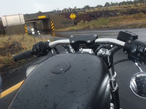 2002 Harley-Davidson XL Sportster - View from the rider's perspective on a wet road, showing the handlebars and fuel tank of a motorcycle.