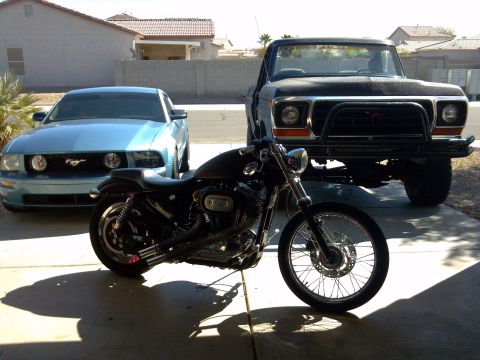 2002 Harley-Davidson XL Sportster - A black motorcycle is parked in a driveway with a blue car and a truck behind it.