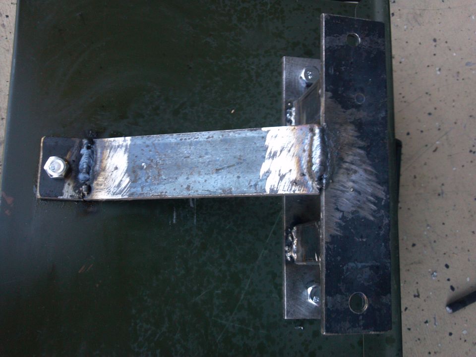 Close-up of a welded metal bracket attached to a dark green surface