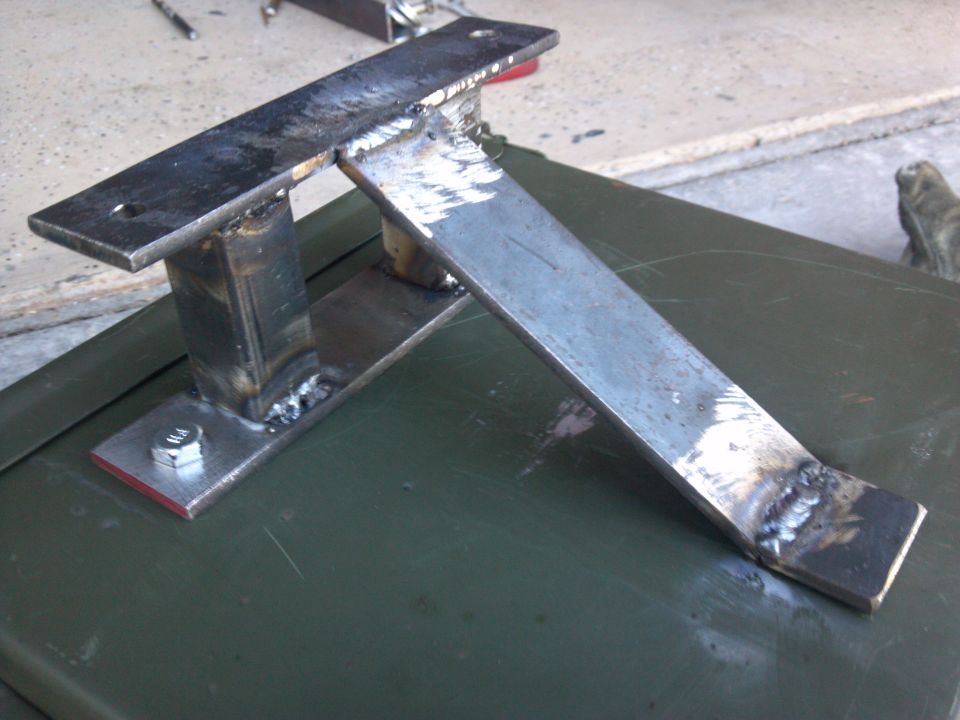 Welded metal bracket with bolt on a green surface. The bracket has a horizontal top plate and an angled support