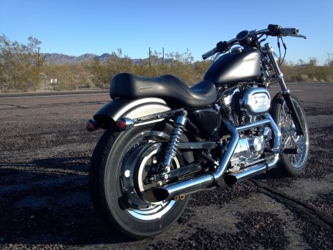 2002 Harley-Davidson XL Sportster - A black Harley-Davidson motorcycle is parked on the side of a road, with a desert landscape in the background under a clear blue sky.