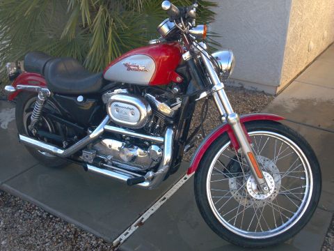 2002 Harley-Davidson XL Sportster - A red and silver 2002 Harley-Davidson XL Sportster motorcycle is parked outside on a sunny day.