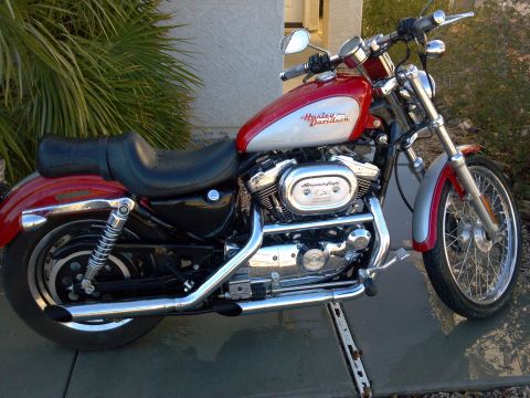 2002 Harley-Davidson XL Sportster - Side view of a red and silver 2002 Harley-Davidson XL Sportster motorcycle parked outdoors.