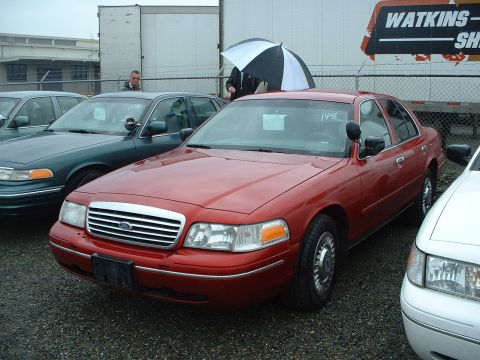 1999 Ford Crown Victoria - Several Crown Victoria sedans, likely ex-police vehicles, are parked outdoors at an auction.