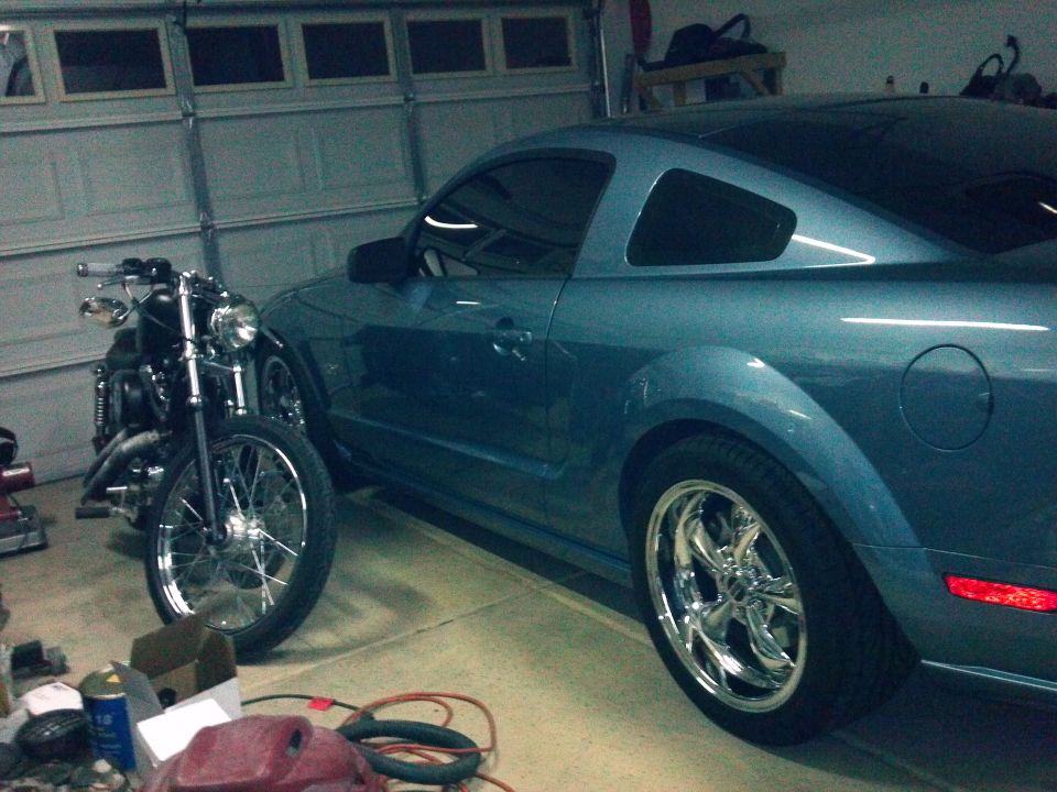 Blue coupe parked next to a motorcycle in a garage