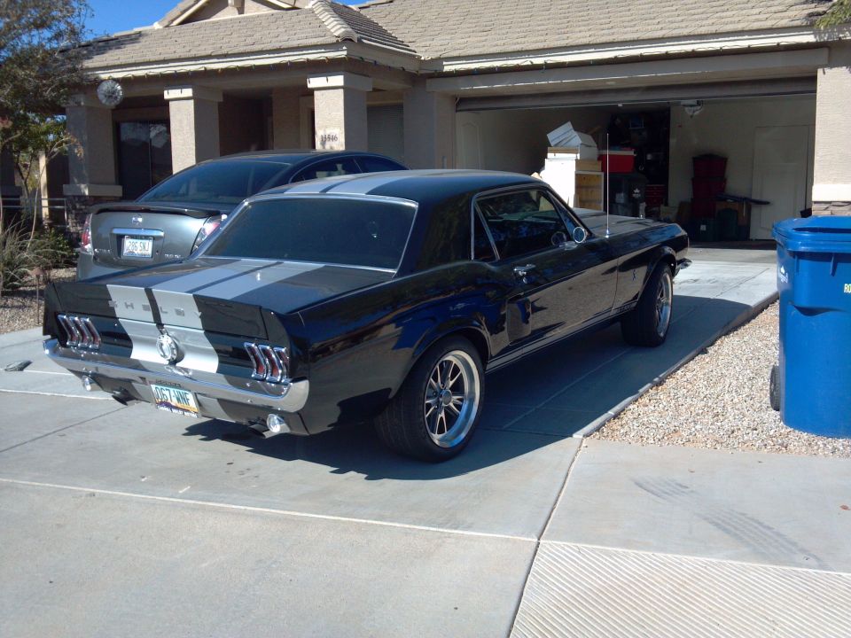 Black 1967-1968 Ford Mustang with silver racing stripes, parked in a driveway