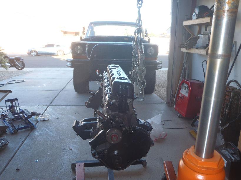 Truck in garage with engine being lifted out. Motorcycle and car parked outside