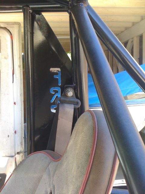 1987 Suzuki Samurai - The interior of a vehicle shows a roll cage, seatbelt, and blue lettering on a black panel.