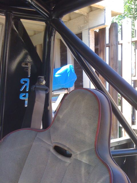 1987 Suzuki Samurai - Close-up of a vehicle's interior, a roll cage and a racing seat with visible blue lettering.