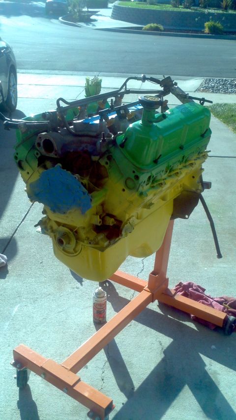 1987 Ford Bronco - An engine is mounted on an orange engine stand, partially painted green and yellow.